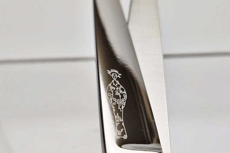 Close-up of a hair scissor blade with a Michiko lady logo engraved on a light gray background