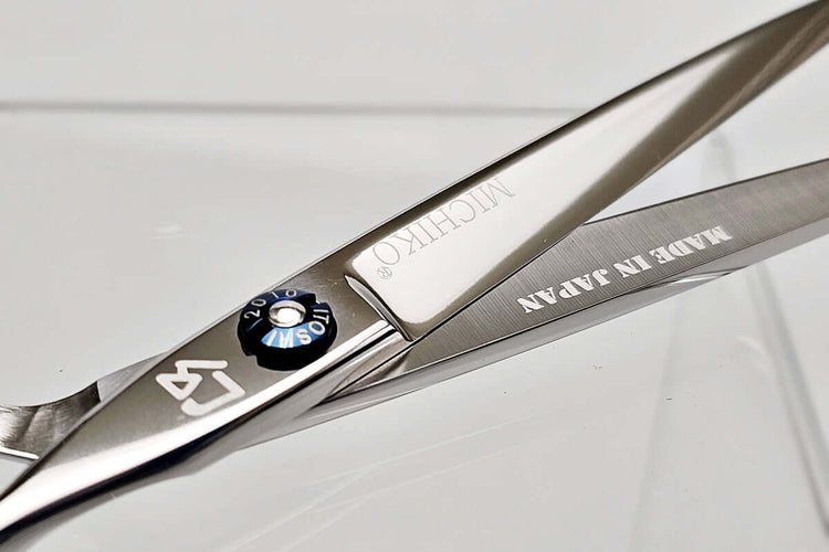 Close-up of a pair of hair scissors with 'Michiko' branding on a light gray background