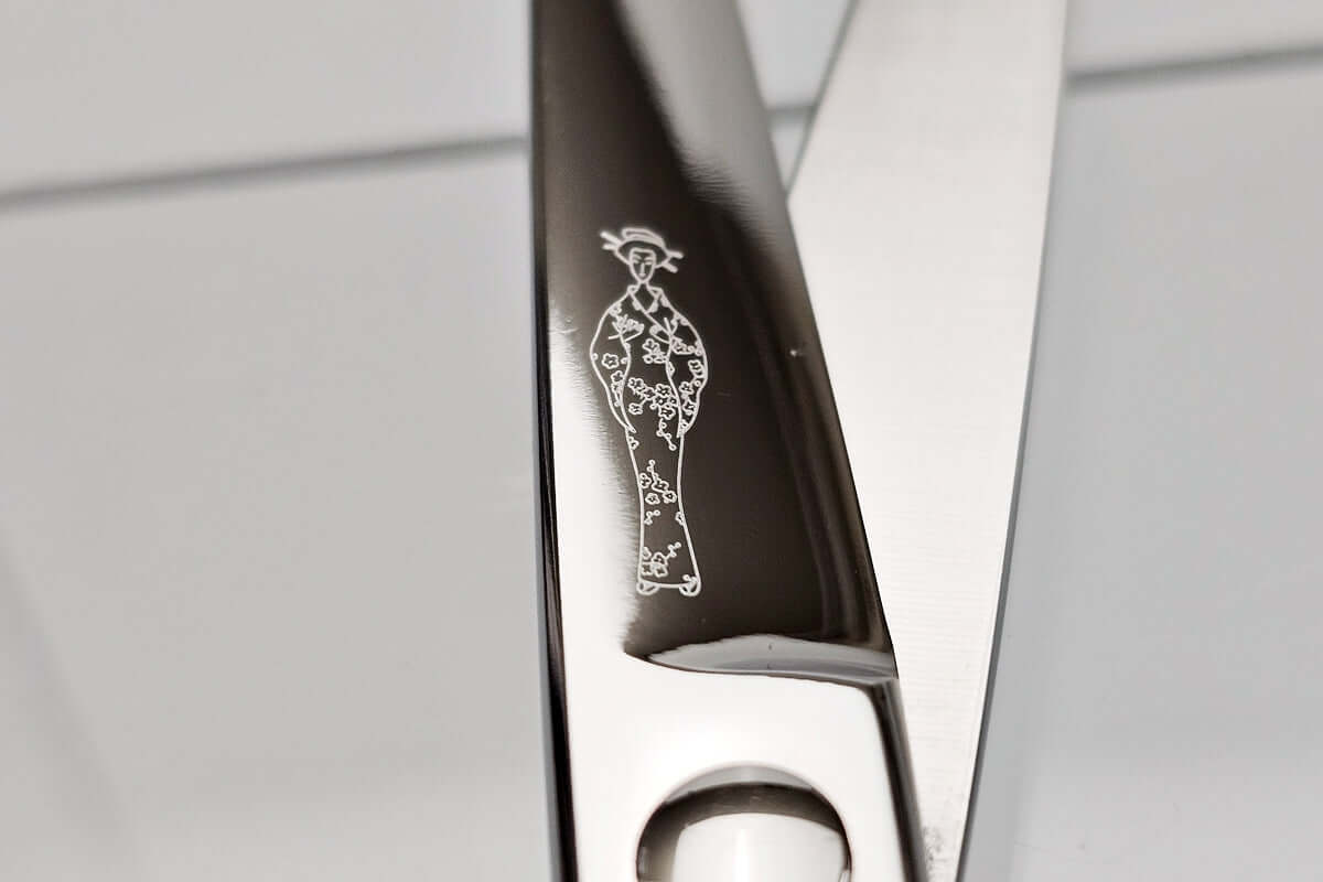Close-up of hair scissors blade with a Michiko lady logo on the blade against a neutral background