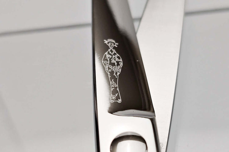 Close-up of hair scissors blade with a Michiko lady logo on the blade against a neutral background