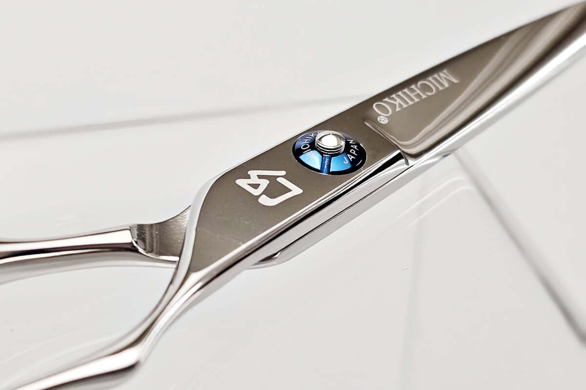 Close-up of a pair of silver hair cutting shears with brand logo on a light gray background