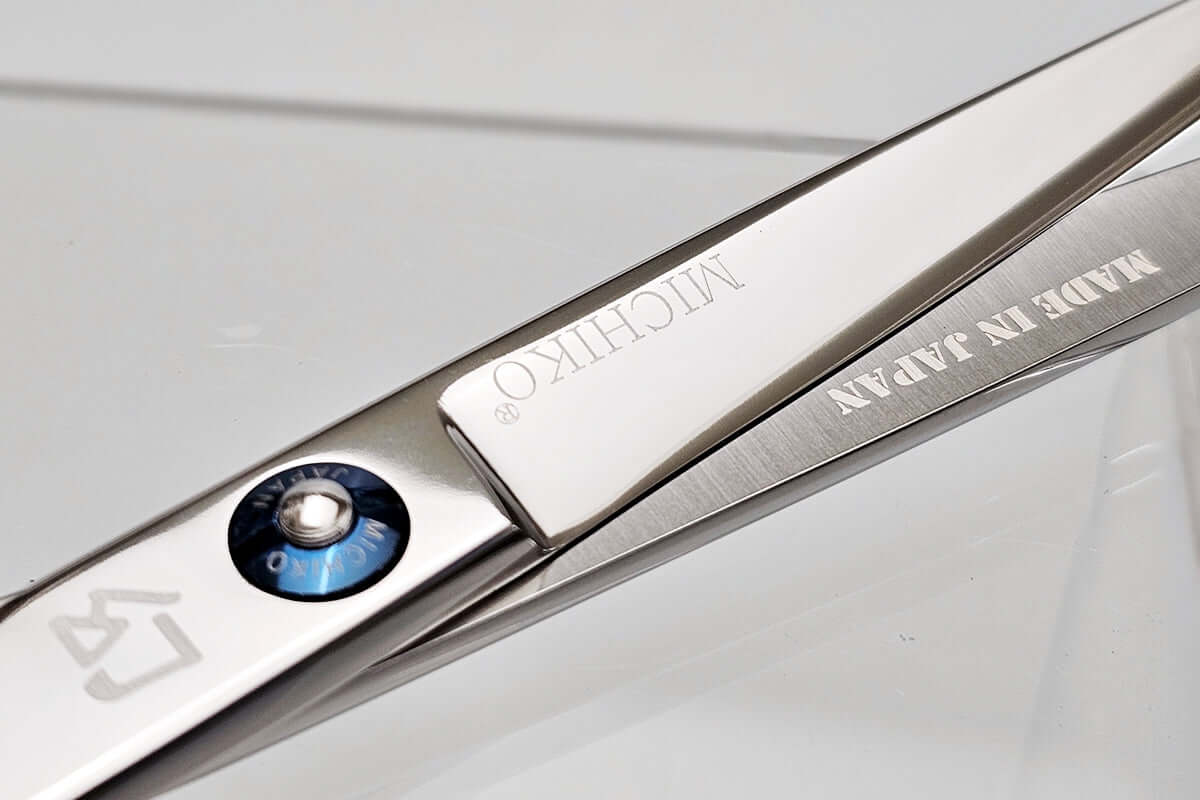 Close-up of a pair of hair scissors with 'MICHIKO' branding with 'Made in Japan' text on a light gray background