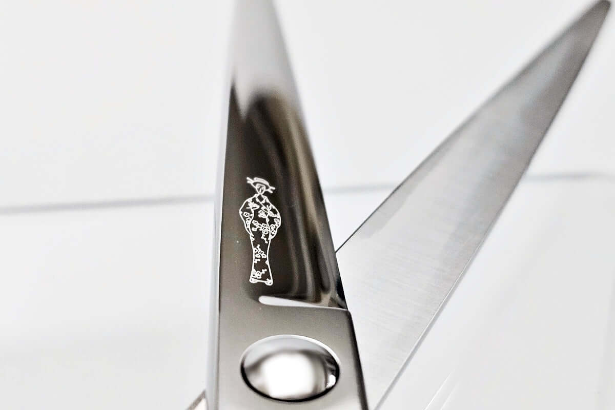 Close-up of a pair of scissors with the MICHIKO lady logo on the blade against a white background