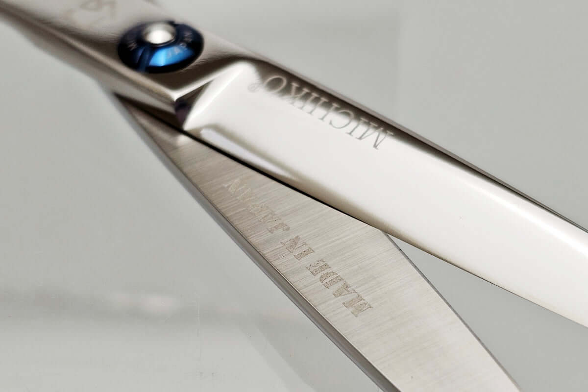 Close-up of a pair of hair scissors blades with 'Michiko' branding on a light gray background