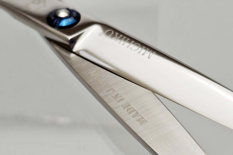 Close-up of a pair of hair scissors blades with 'Michiko' branding on a light gray background