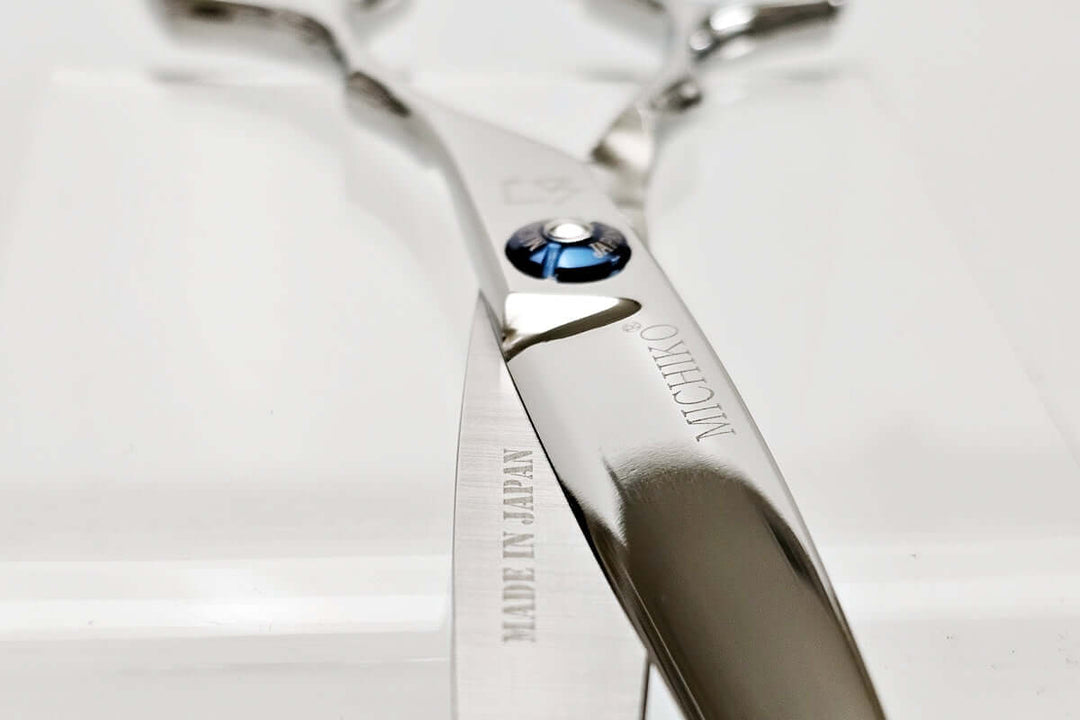 Close-up of a pair of silver hair scissors with a brand logo on a light background