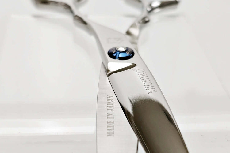 Close-up of a pair of silver hair scissors with a brand logo on a light background