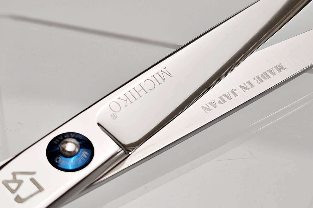 Close-up of a pair of hair scissors with 'MICHIKO' branding on a light gray background