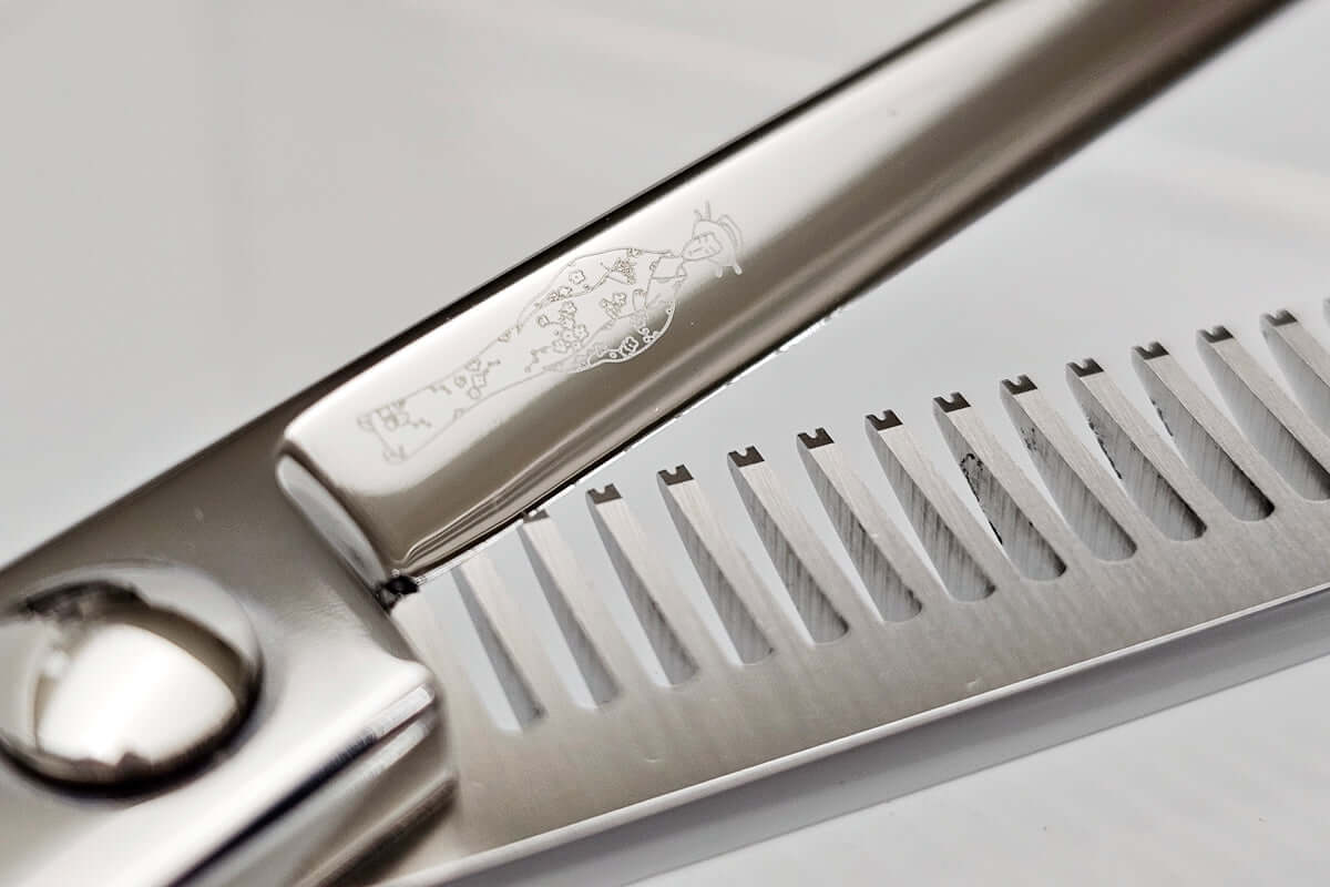 Close-up of hair-thinning scissors blade with engraved MICHIKO lady logo on a light gray background