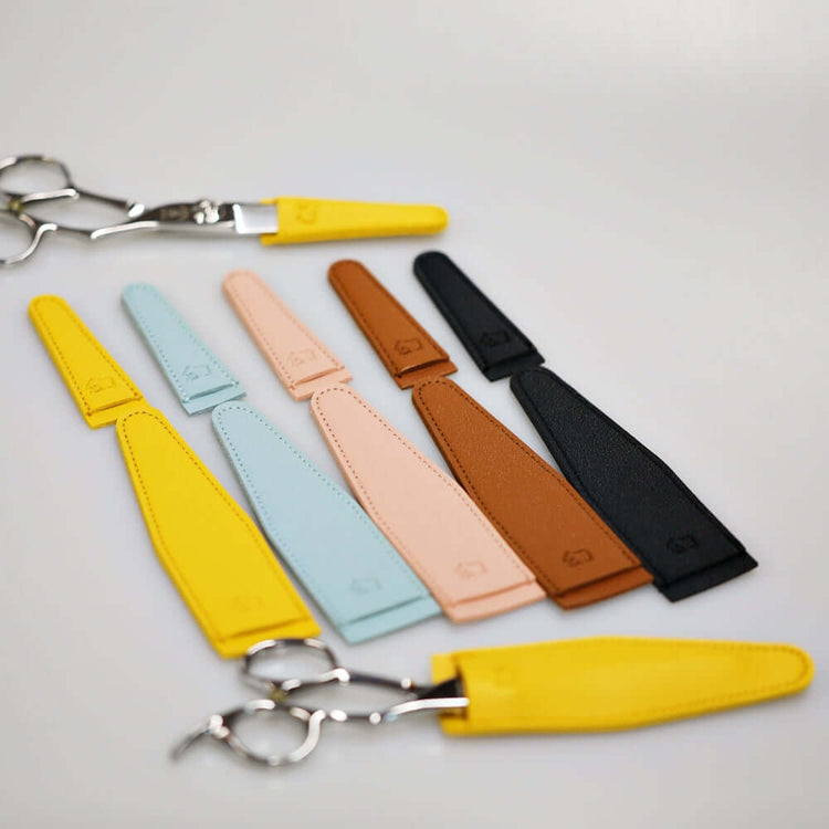 Small and large hair scissors tip covers in five colors (black, blue, pink, yellow, and brown), demonstrating usage with two scissors, each fitted with different size tip covers.